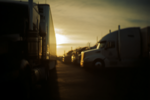 FMCSA Training Provider Registry Crackdown – Sweeping 2025 Enforcement Removes 244 Providers 6 Row of parked semi-trucks at sunrise with warm golden light reflecting off their trailers in a truck stop lot.