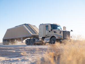 Autonomous frac sand truck equipped with Kodiak Driver hauling a trailer along a dusty lease road in the Permian Basin.