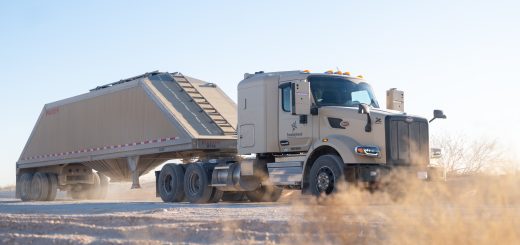 Autonomous frac sand truck equipped with Kodiak Driver hauling a trailer along a dusty lease road in the Permian Basin.
