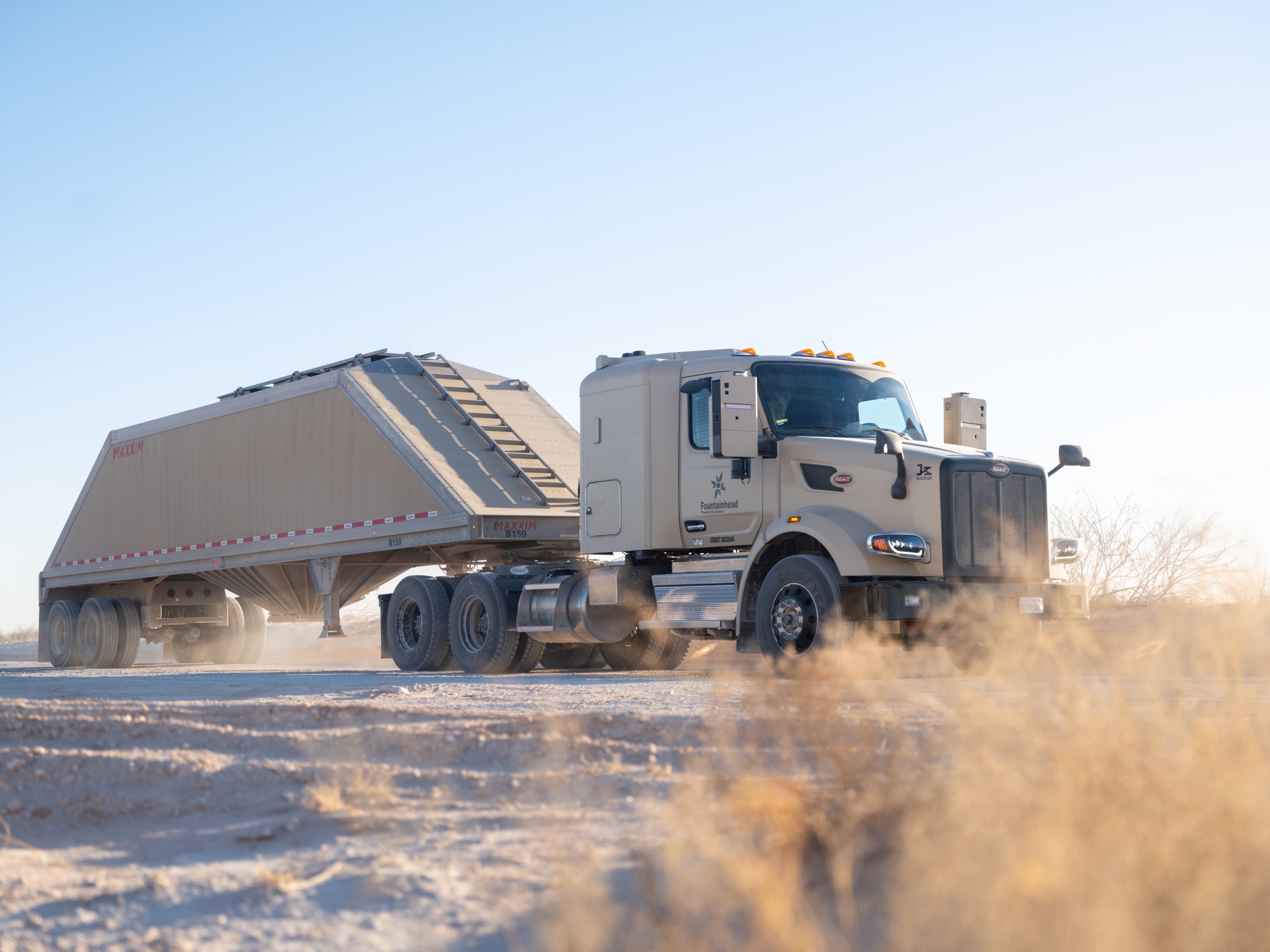 Autonomous frac sand truck equipped with Kodiak Driver hauling a trailer along a dusty lease road in the Permian Basin.