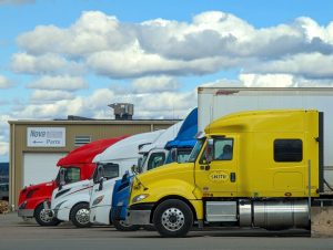 Row of brightly colored semi trucks parked outside a truck center on an overcast day.