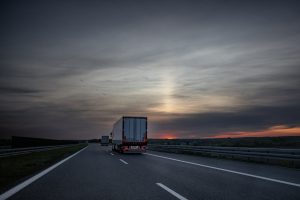 Multiple semi trucks driving along a multi‑lane highway at sunset.