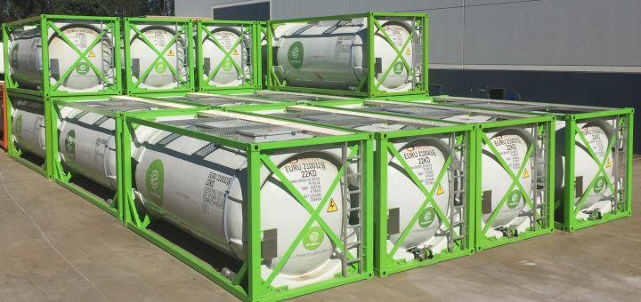 Rows of white OmniTAINER portable tanks in green Eurotainer intermodal frames outside an industrial building