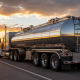 Stainless steel tanker truck traveling on a highway at sunset with a dramatic sky and open road.