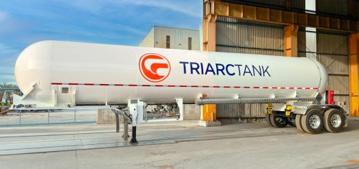 White TriArc MC 331 LPG tank trailer with tandem axles parked outside a manufacturing building.