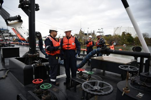 Two Coast Guard officials in hard hats reviewing printed documents on a barge deck