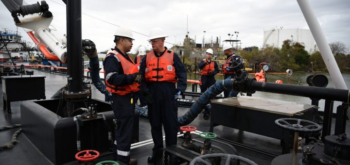 Two Coast Guard officials in hard hats reviewing printed documents on a barge deck