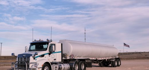 White tractor with a silver fuel cargo-tank trailer parked in a Texas landscape under clear skies