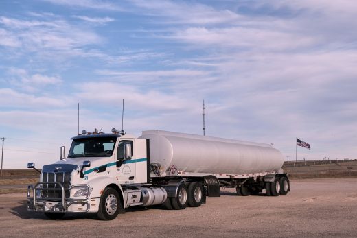 White tractor with a silver fuel cargo-tank trailer parked in a Texas landscape under clear skies