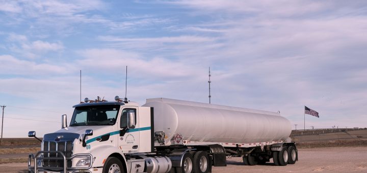 White tractor with a silver fuel cargo-tank trailer parked in a Texas landscape under clear skies