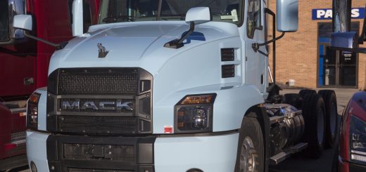 Light-blue Mack Anthem daycab tractor parked among other trucks outside a dealership.