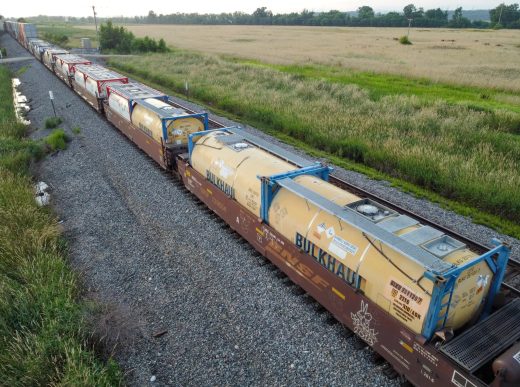 Yellow Bulkhaul and other ISO tank containers carried on BNSF railcars beside open fields.