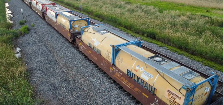 Yellow Bulkhaul and other ISO tank containers carried on BNSF railcars beside open fields.