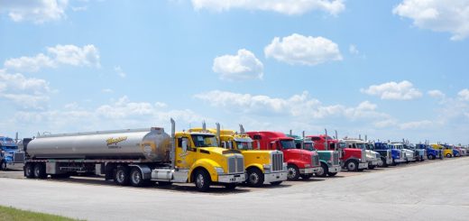 Row of fuel tanker trucks with yellow, red and blue cabs parked on an airfield apron.